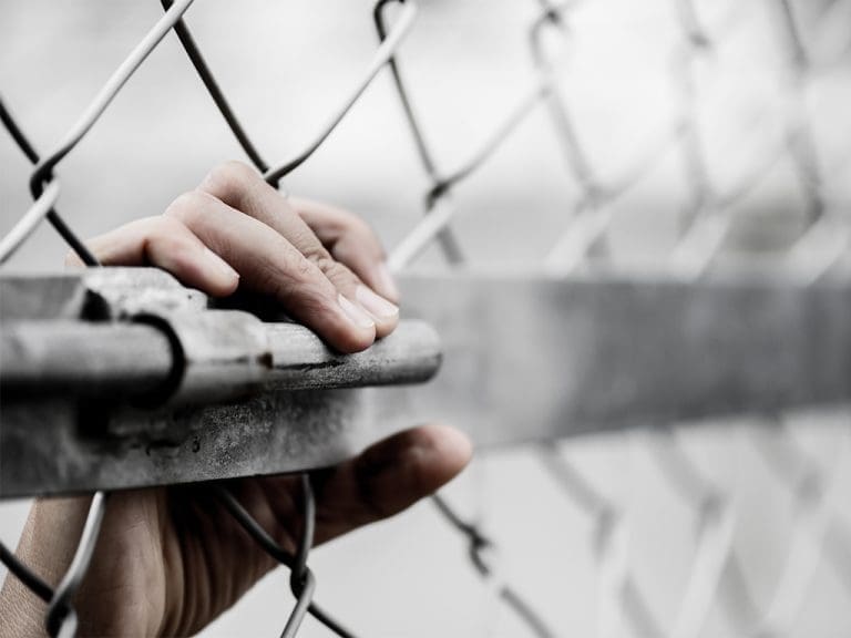 Aufmacherbild zum Lieferkettengesetz. Eine Hand greift an einen Maschendrahtzaun.