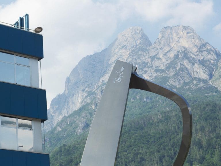 Firmensitz von EssilorLuxottica in Agordo, Italien und Ray-Ban-Fassung jeweils angeschnitten zu sehen