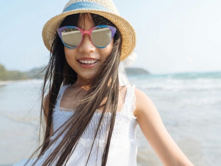 Mädchen mit Sonnenbrille und Sonnenhut lacht in die Kamera