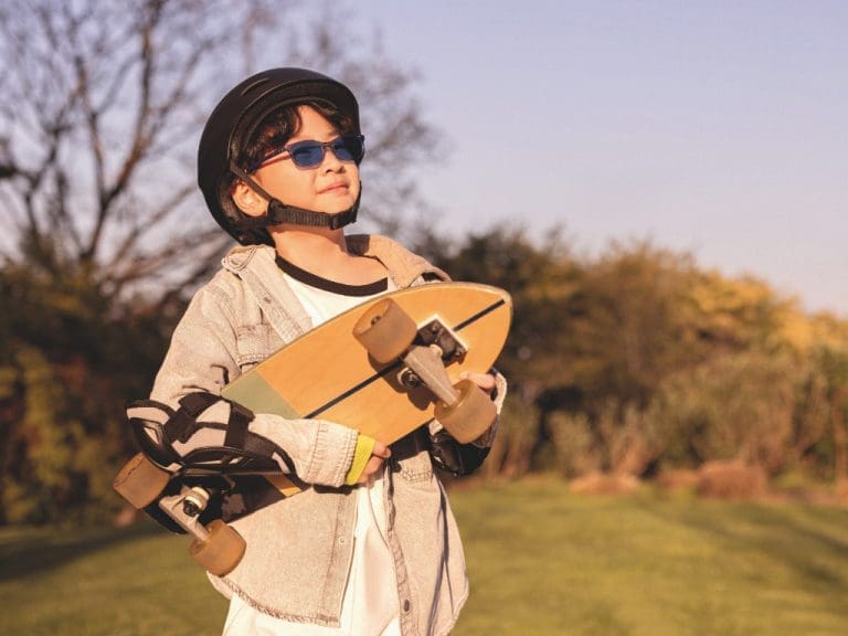 Kind trägt Essilor Stellest Sonnenbrille und hat Skateboard im Arm
