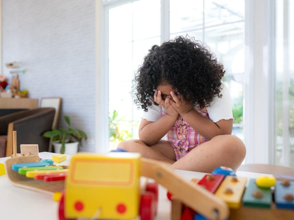 Kleines Mädchen sitzt traurig da und bedeckt ihr Gesicht mit den Händen