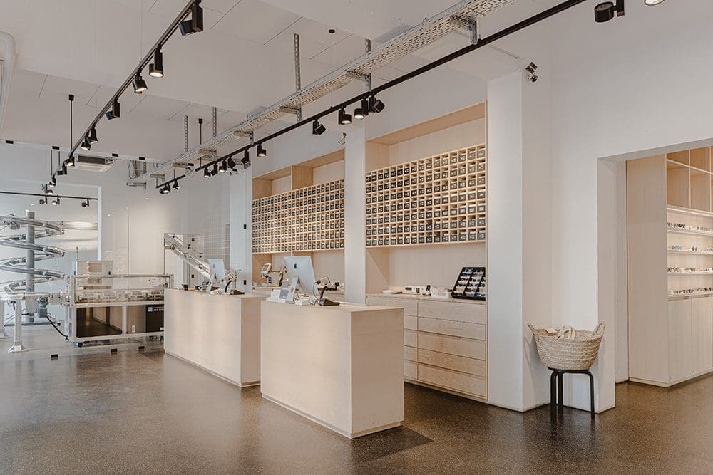 Das Bild zeigt die hochmoderne Innenansicht eines augenoptischen Fachgeschäftes. Die Ladeneinrichtung ist farblich in Weiß mit hellen Holzakzenten gehalten.