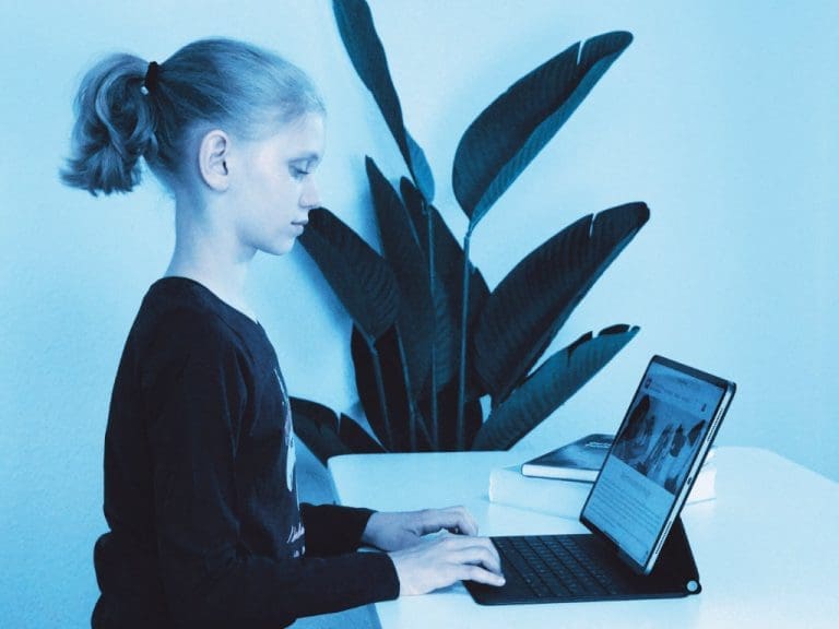 Mädchen im Schulalter sitzt an Tisch und schreibt auf Tablet-Tastatur