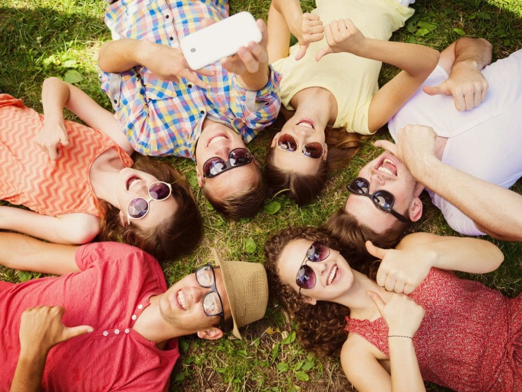 Lächelnde Runde an Personen liegt im Kreis auf einer Wiese und trägt Sonnenbrillen