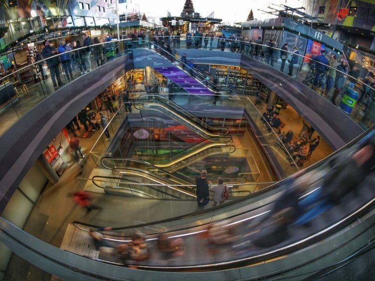 Innenaufnahme in einem Shopping-Center zeigt Menschen verschwommen auf einer Rolltreppe