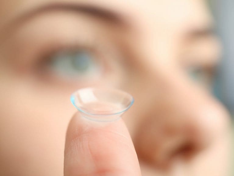 Frau hält Kontaktlinse auf dem Finger vor dem Gesicht