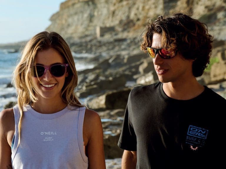 Weibliches und männliches Model tragen O’Neill-Sonnenbrillen am Strand.