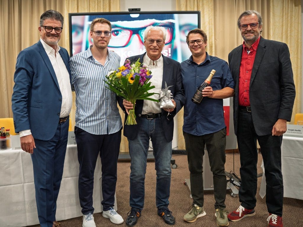 Emotionale Verabschiedung von Klaus Hogrebe (Mitte) nach 27 Jahren ehrenamtlicher Arbeit im Vorstand der IGA Optic-Genossenschaft. Geschäftsführer Carsten Schünemann (links) und Aufsichtsratschef Ralph Hurlin (rechts) überraschten ihn auf dem IGA Optic Unternehmertag 2025 mit dem Besuch seiner Söhne Christian und André Hogrebe (IGA Optic Mues & Sternemann in Recklinghausen und Oer-Erkenschwick