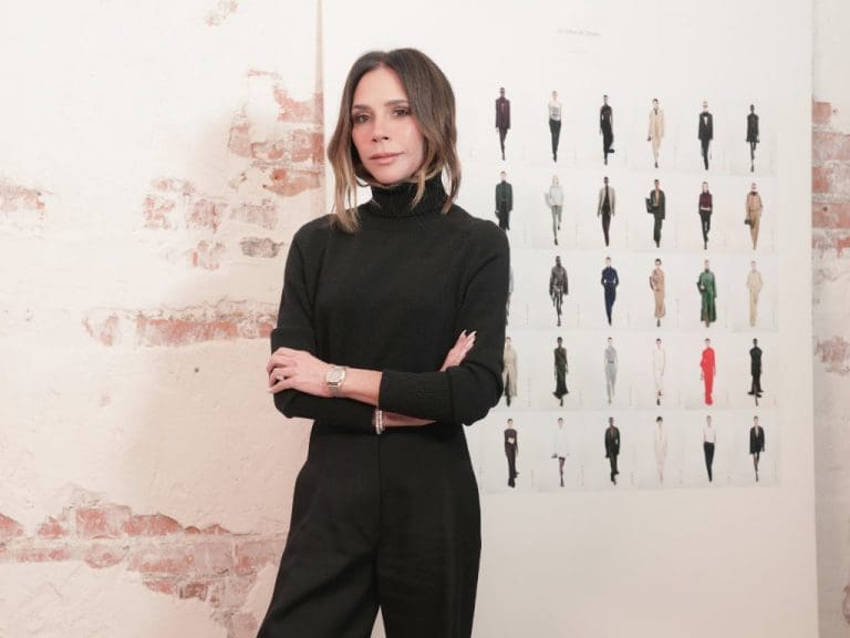Victoria Beckham steht vor einer Leinwand mit mehreren Modeskizzen