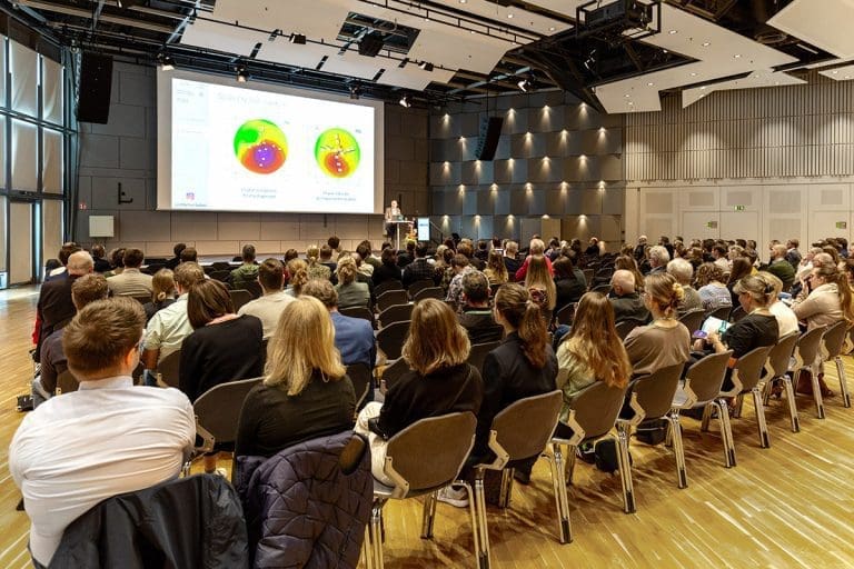 Vortragsszene auf dem Optometrie-Kongress SICHT.KONTAKTE 2022 in Osnabrück, mit Referent am Pult und Publikum im Saal.
