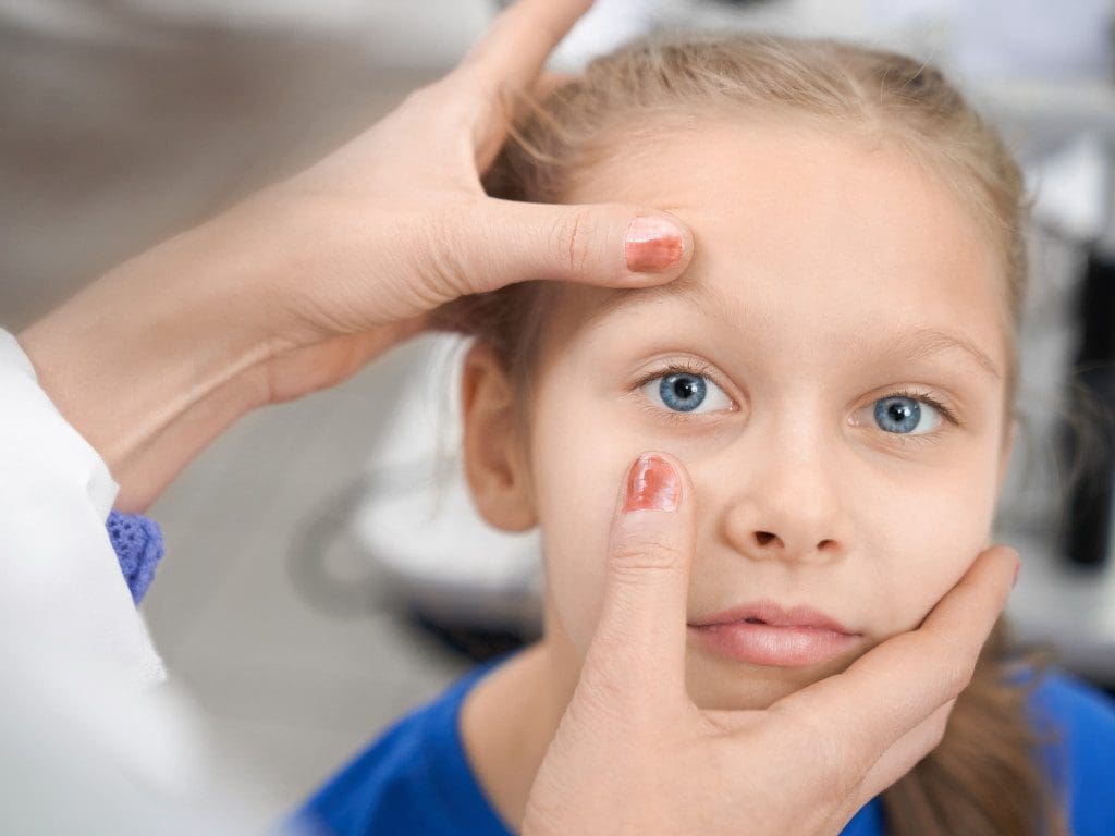 Hübsches Mädchen schaut in die Kamera, während ein Augenoptiker oder Augenarzt das Sehvermögen überprüft.