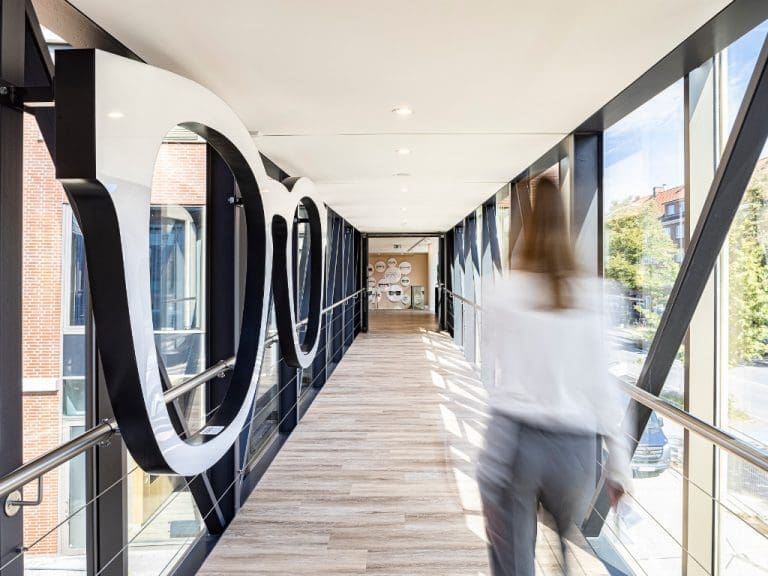 Schemenhafte Frau überquert die aus zwei Gebäuden bestehende neue Fielmann-Zentrale über eine Brücke an deren Wand eine große Brille als Symbol für das Unternehmen Fielmann angebracht ist