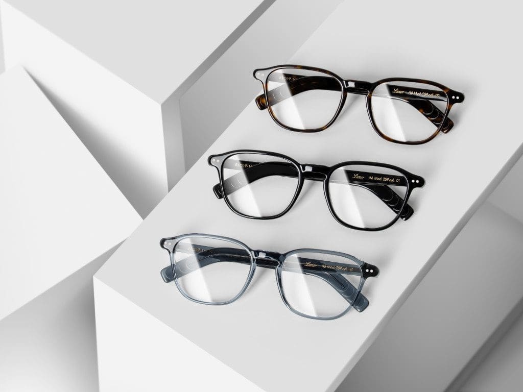 Drei Acetat-Brillen von Lunor mit transparenten Gläsern und dunklen Fassungen, die auf einer weißen, geometrischen Oberfläche liegen