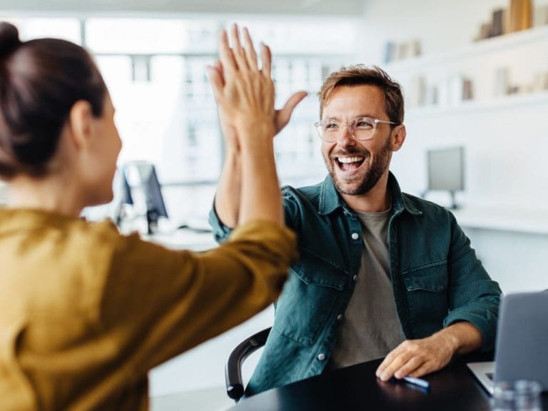 Glücklicher Mann mit Brille klatscht Frau ab, die nur von hinten zu sehen ist.