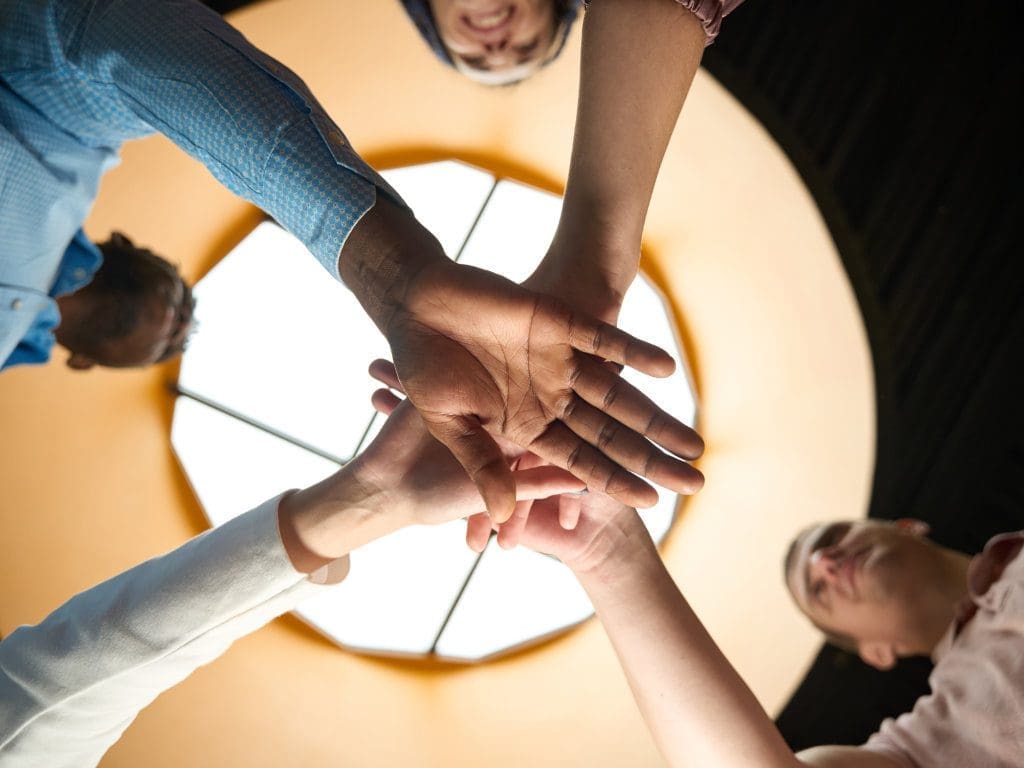 Engagiertes Team, das als Symbol zur Zusammenarbeit die Hände zusammenlegt