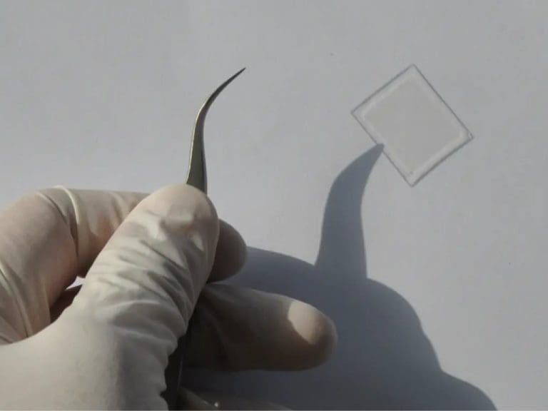 Hand, die mit einer Pinzette ein Glasstück hält