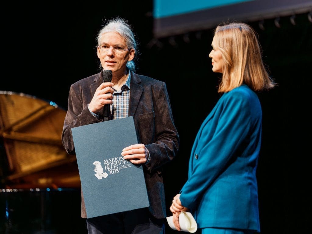 EinDollarBrille-Vereinsgründer Martin Aufmuth nimmt den Marion-Dönhoff-Preis auf der Bühne im Deutschen Schauspielhaus Hamburg entgegen, neben ihm steht Julia-Niharika Sen, Moderatorin der Preisverleihung