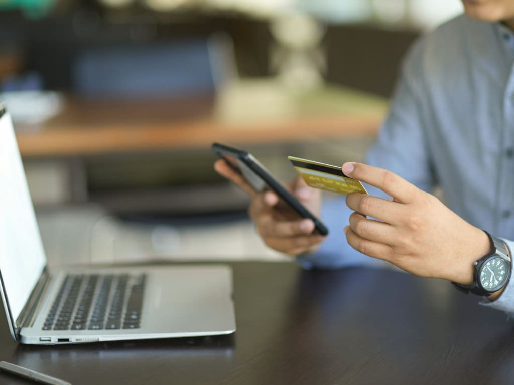 Mann beim Online-Einkauf mit Laptop, Kreditkarte und Handy